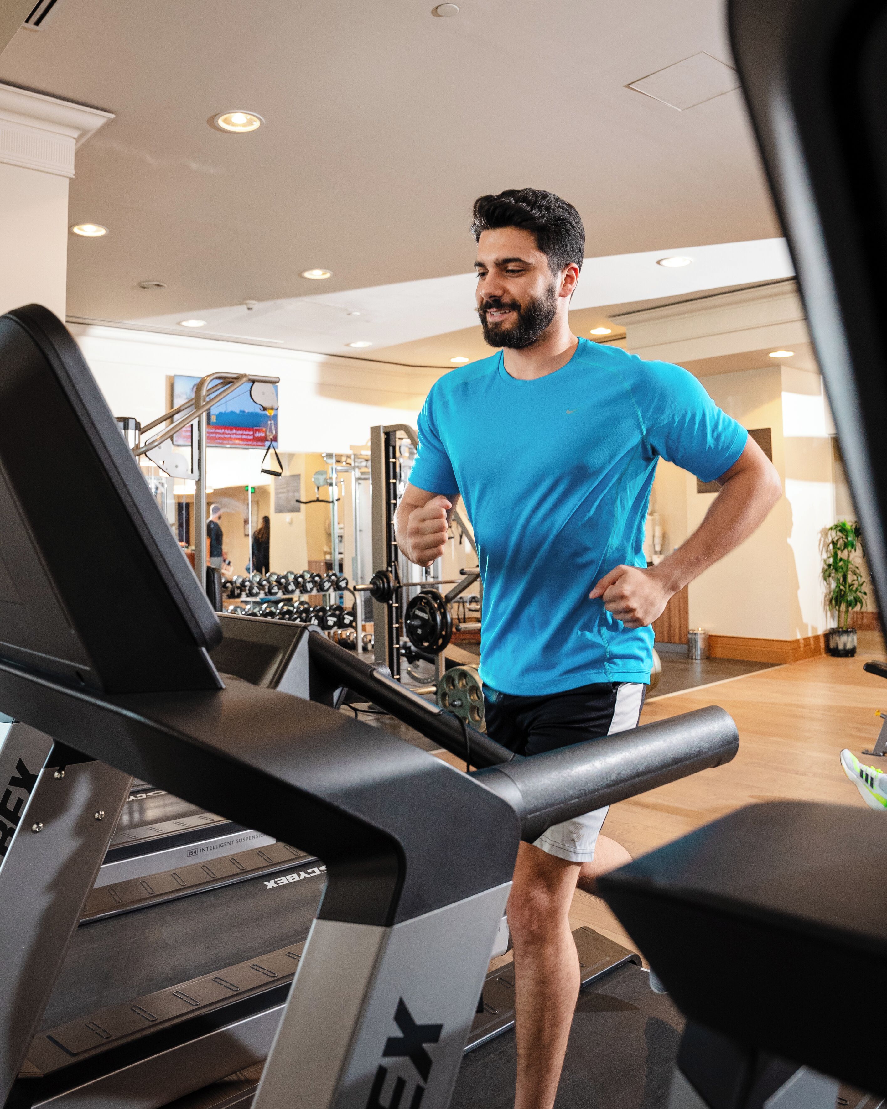 A man running on a treadmill in a gym with exercise equipment and a mirror in the background.