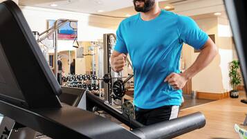 A man running on a treadmill in a gym with exercise equipment and a mirror in the background.