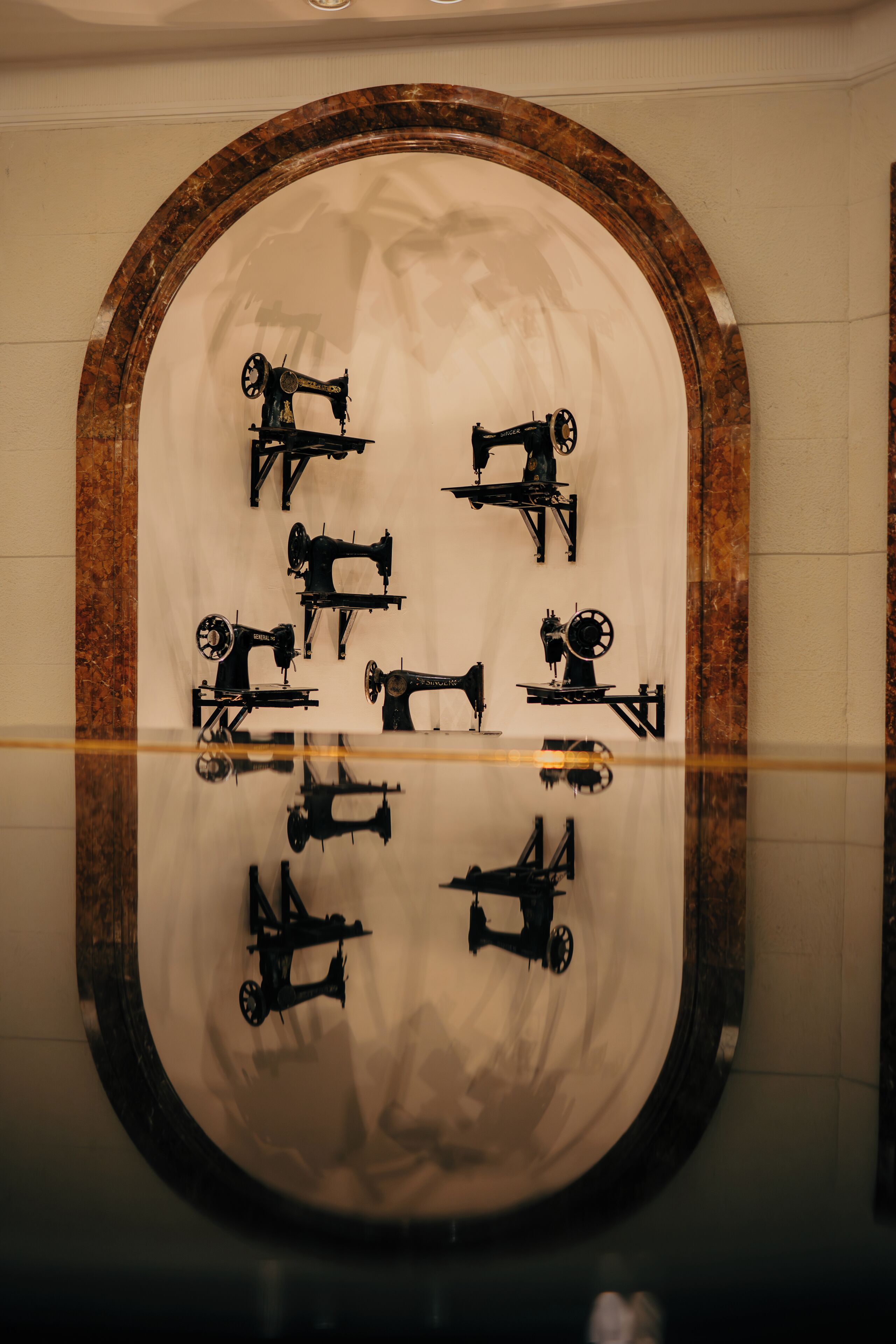 A circular mirror with a wooden frame reflecting six sewing machines.