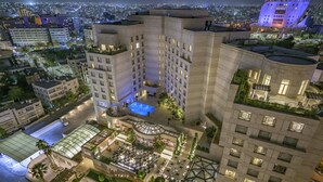 A high-rise hotel with multiple floors, a rooftop pool, and a landscaped courtyard with seating areas. - Grand Hyatt Amman (Amman)
