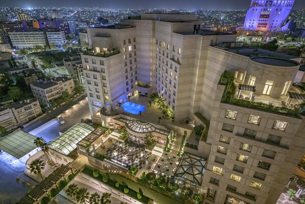 Un hotel de gran altura con múltiples pisos, una piscina en la azotea y un patio ajardinado con zonas de estar.