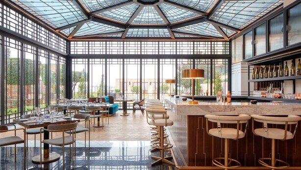 A spacious restaurant with a high ceiling, large windows, and a bar area with stools. - Grand Hyatt Amman (Amman)