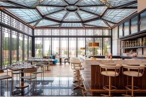 A spacious restaurant with a high ceiling, large windows, and a bar area with stools. - Grand Hyatt Amman (Amman)