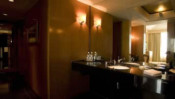 A hotel bathroom with a large mirror, two sinks, and a vanity with toiletries.