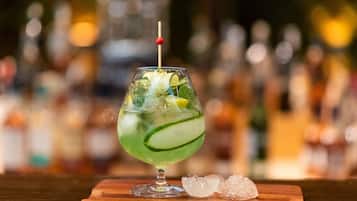 A cocktail with lime and mint garnish, served in a glass with a straw, on a wooden coaster with ice cubes beside it.