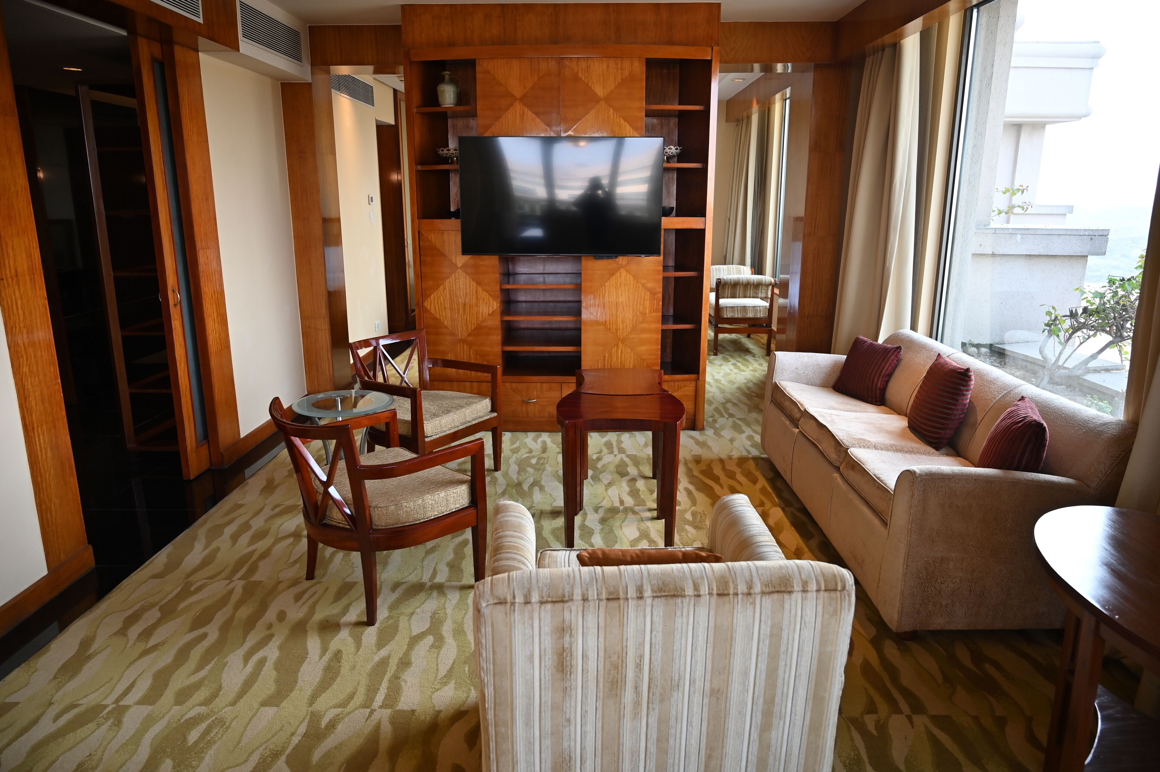 A living room with a flat-screen TV, wooden furniture, a sofa, and a view of the outdoors.