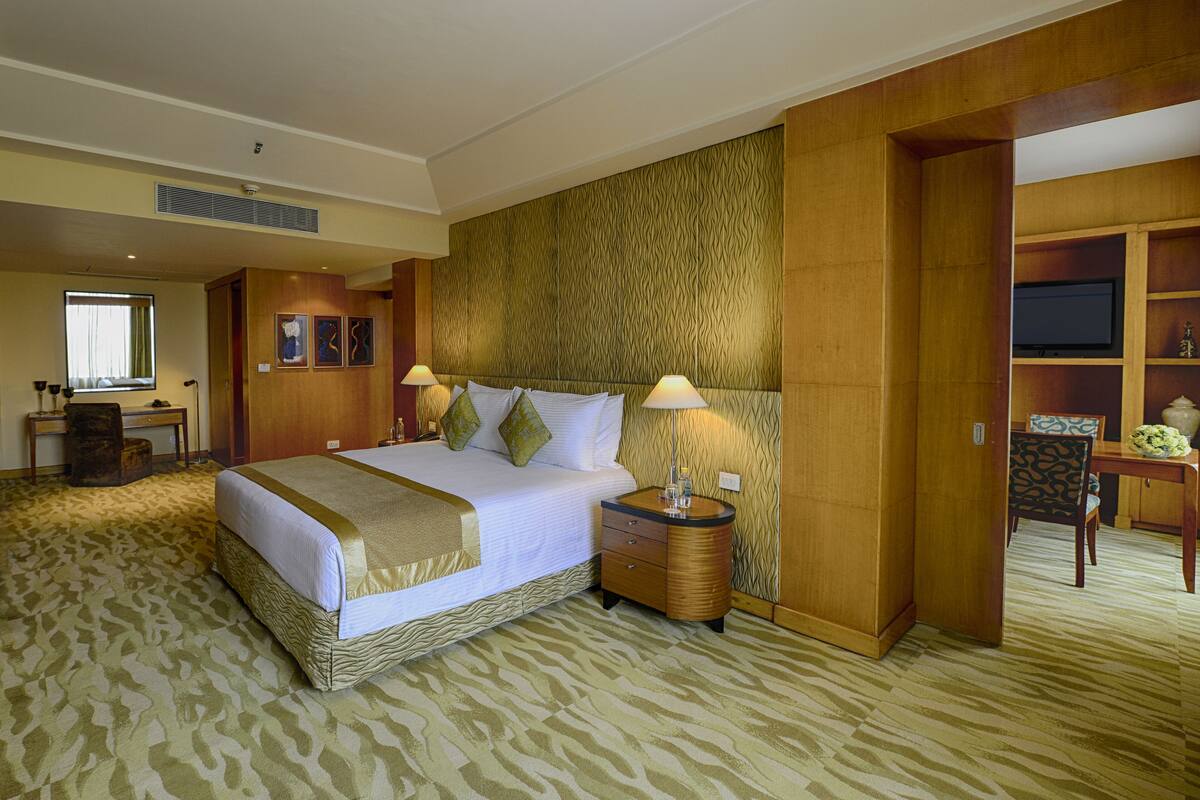 A hotel room with a large bed, a desk, a chair, a TV, and a wooden cabinet.