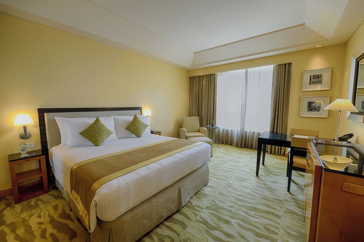 A hotel room with a large bed, a desk, a chair, a lamp, and a window with curtains.