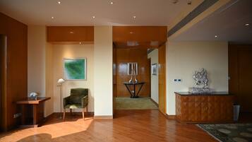 A spacious room with wooden flooring, a green armchair, a small table, a cabinet with a statue, and a painting on the wall.