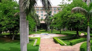 Un giardino curato con fontana centrale, palme e un edificio sullo sfondo.