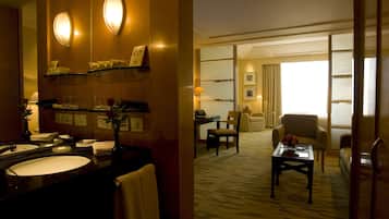 A hotel room with a bathroom, a sitting area with a coffee table, and a view through a window.