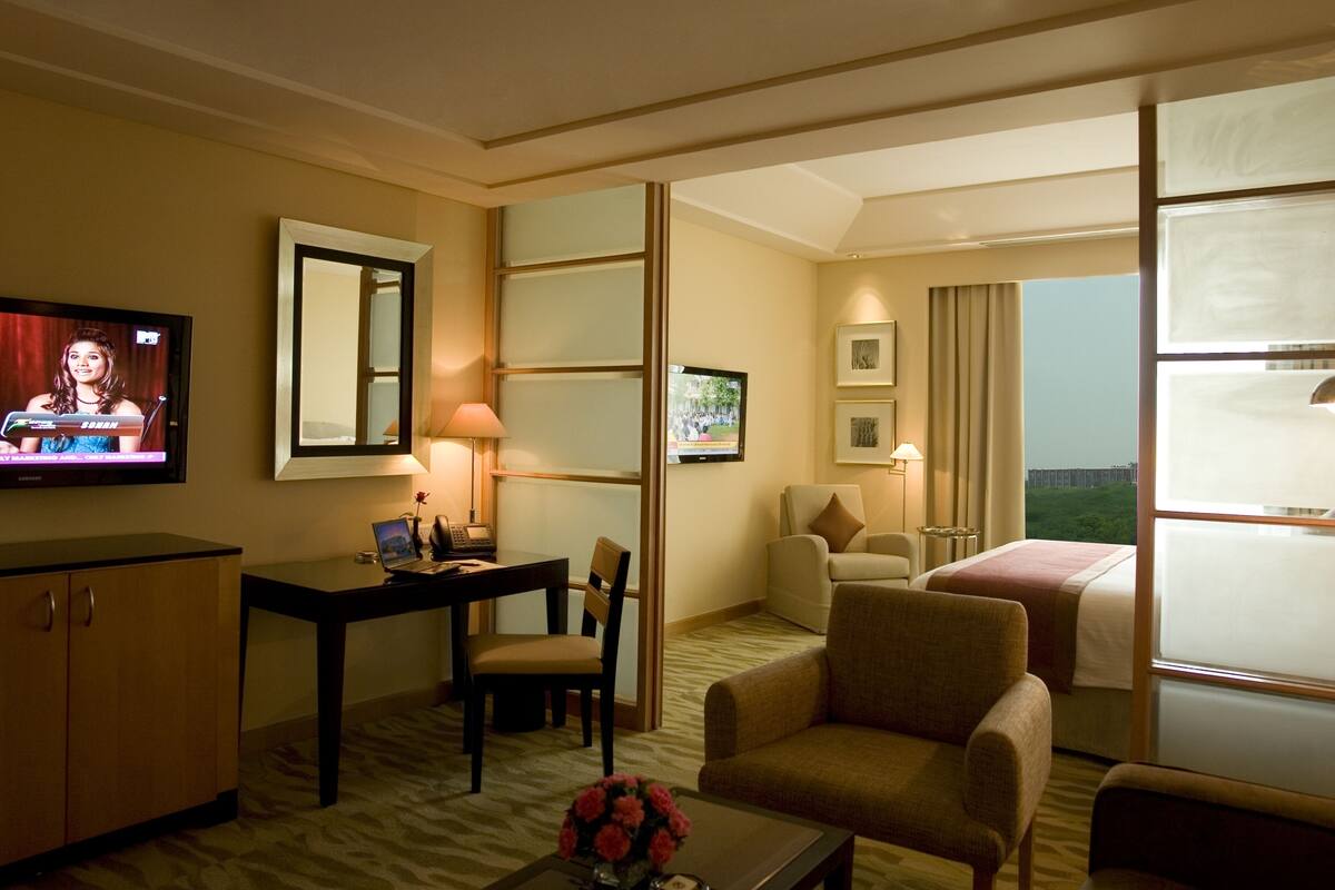 A hotel room with a television, desk, chair, sofa, and bed.