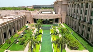 Un grande edificio con un cortile centrale che presenta un prato verde, palme e una piscina.