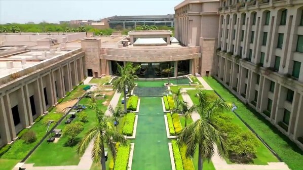 A large building with a central courtyard featuring a green lawn, palm trees, and a swimming pool. - The Grand New Delhi (New Delhi)
