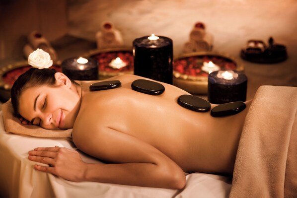 A person receiving a hot stone massage with candles and a flower in a spa setting.