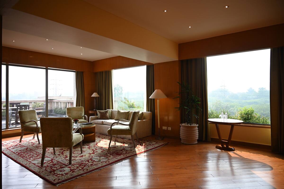 A spacious living room with a large window, a sofa, chairs, a coffee table, and a lamp.