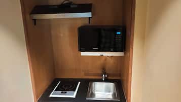 Una kitchenette compacta con microondas integrado, hornilla y pileta.