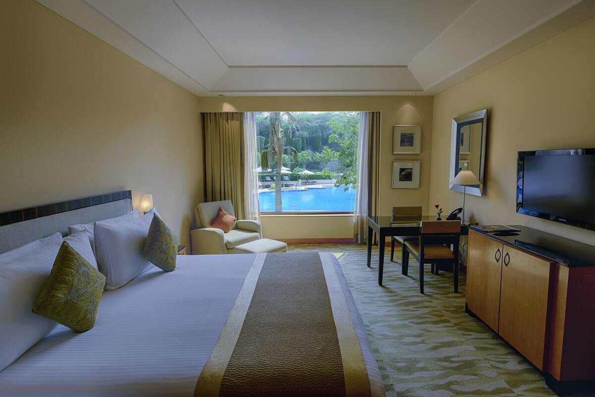 A hotel room with a bed, a desk, a television, and a view of a swimming pool.
