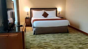 Una habitación de hotel con cama, lámparas de noche, televisor y alfombra estampada.