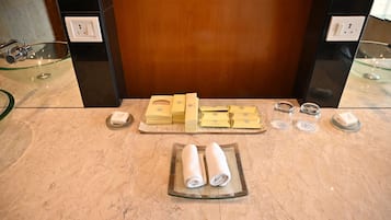 A hotel bathroom with a marble countertop, glass bowl sink, and toiletries arranged on the counter.