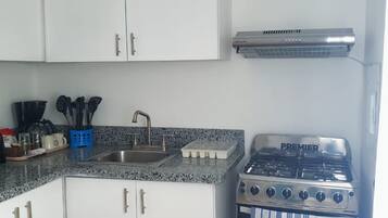 A compact kitchen with white cabinets, a gas stove, and a stainless steel range hood.