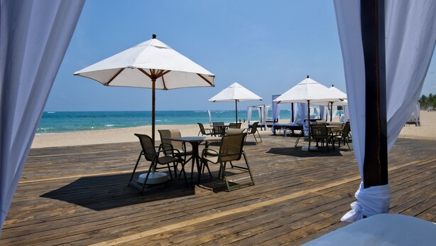 Un restaurante frente al mar con terraza al aire libre, sombrillas blancas y una cubierta de madera.