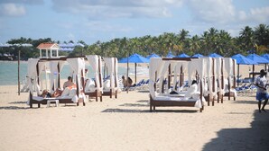 Una playa con filas de toldos blancos y sombrillas azules, algunas ocupadas por personas.