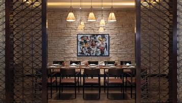 A restaurant with a stone wall, a large abstract painting, and a set dining table with chairs.