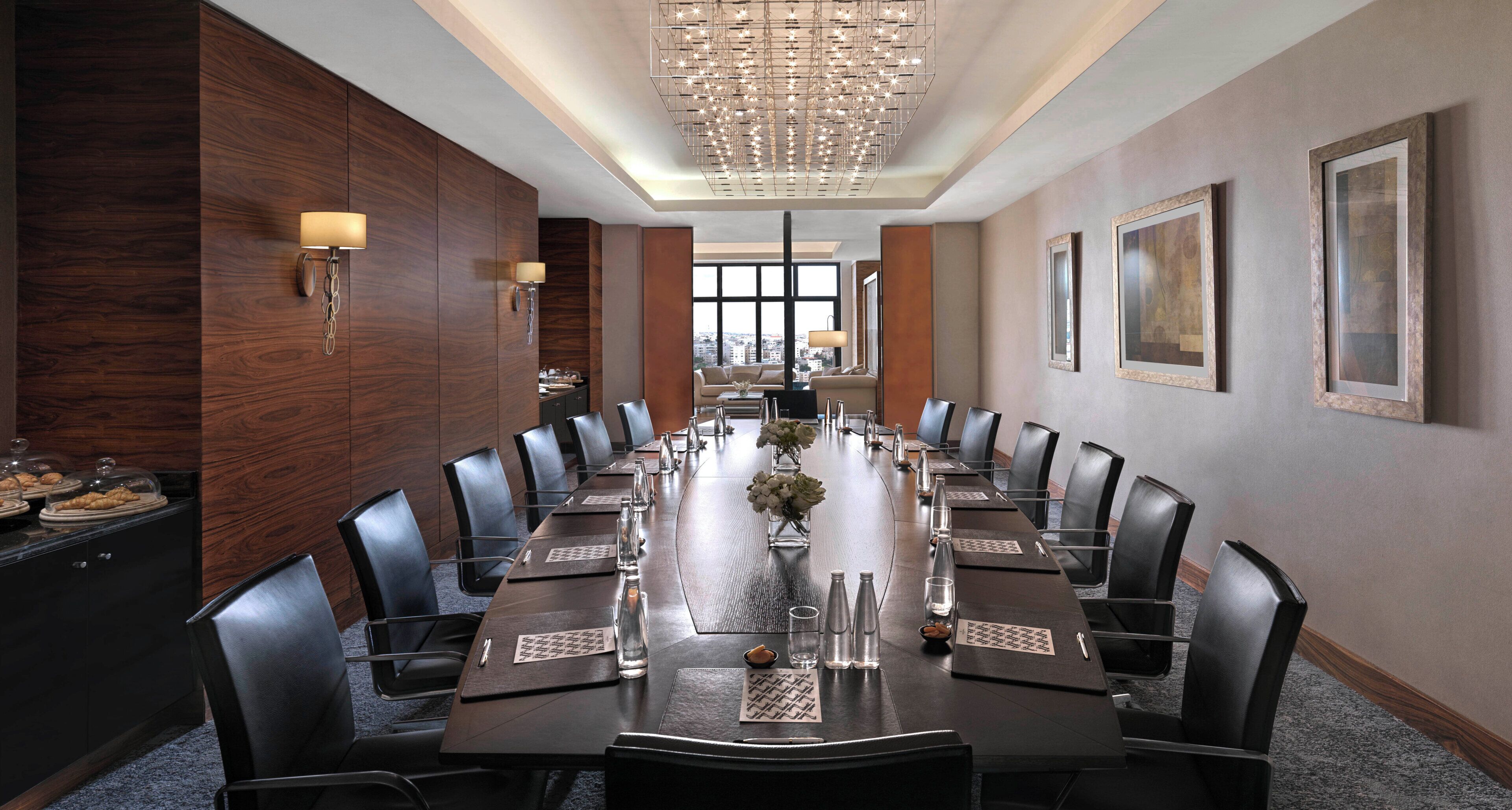 A conference room with a long table, black leather chairs, and a chandelier.