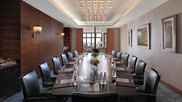 A conference room with a long table, black leather chairs, and a chandelier.
