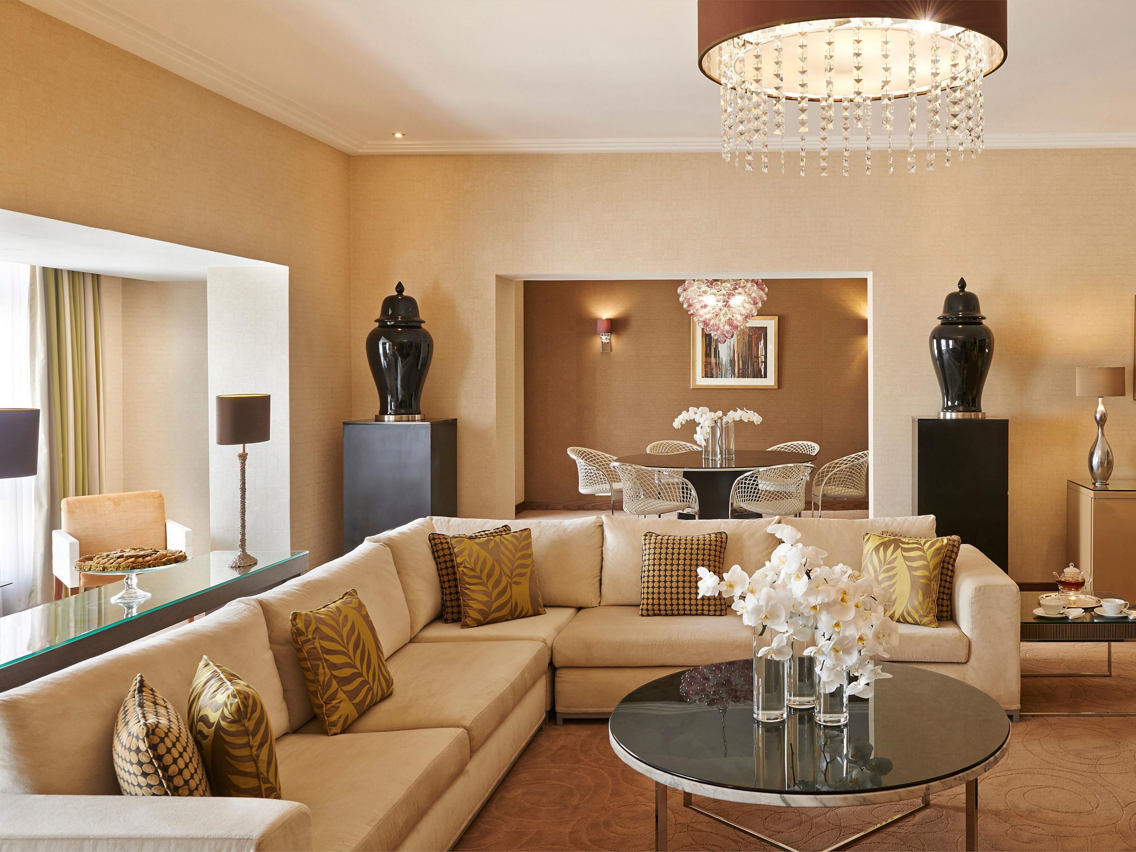 A spacious living room with a large sectional sofa, a round coffee table, and a dining area with a chandelier.
