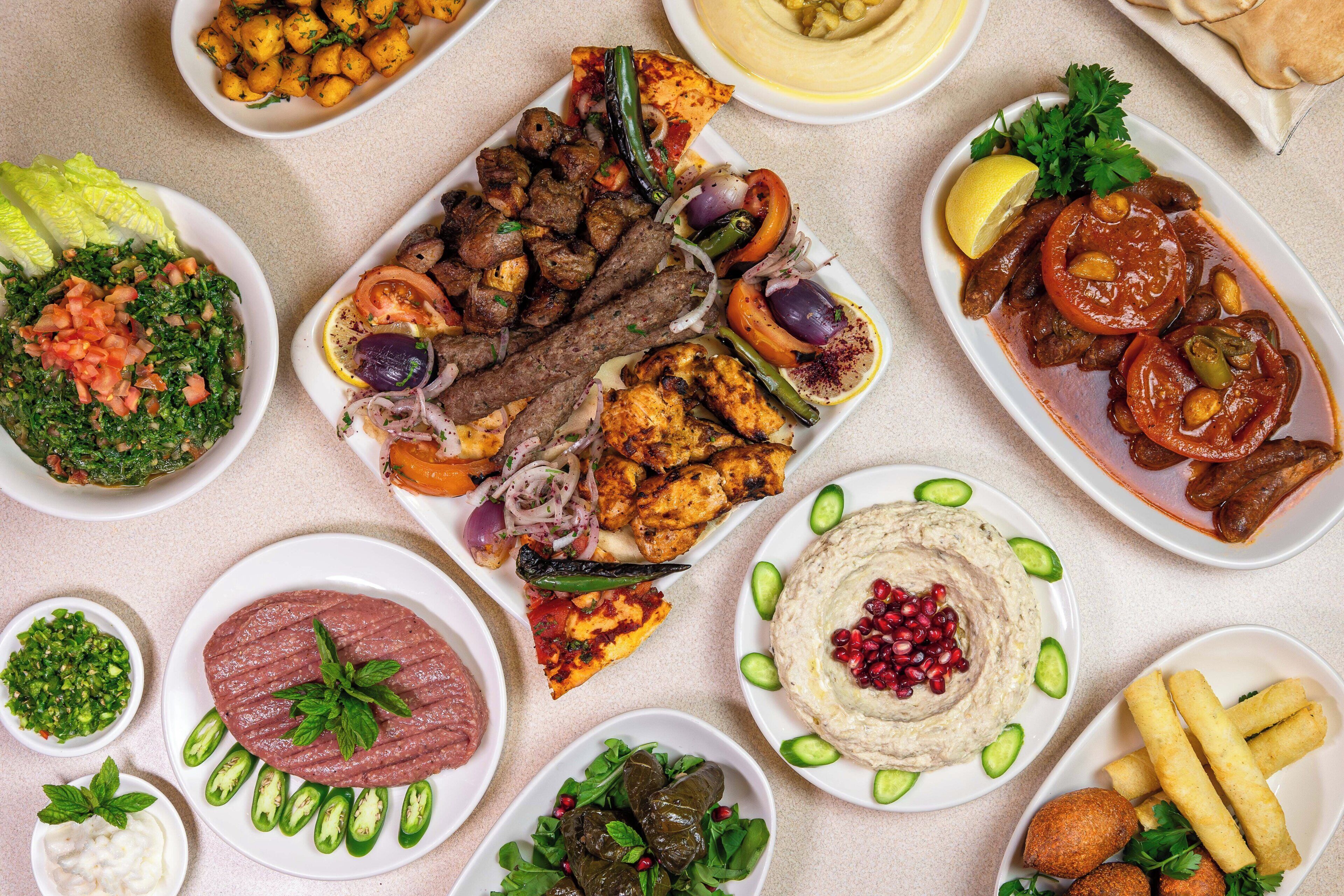 Une variété de plats, notamment des brochettes, du houmous et des salades, disposés sur une table.