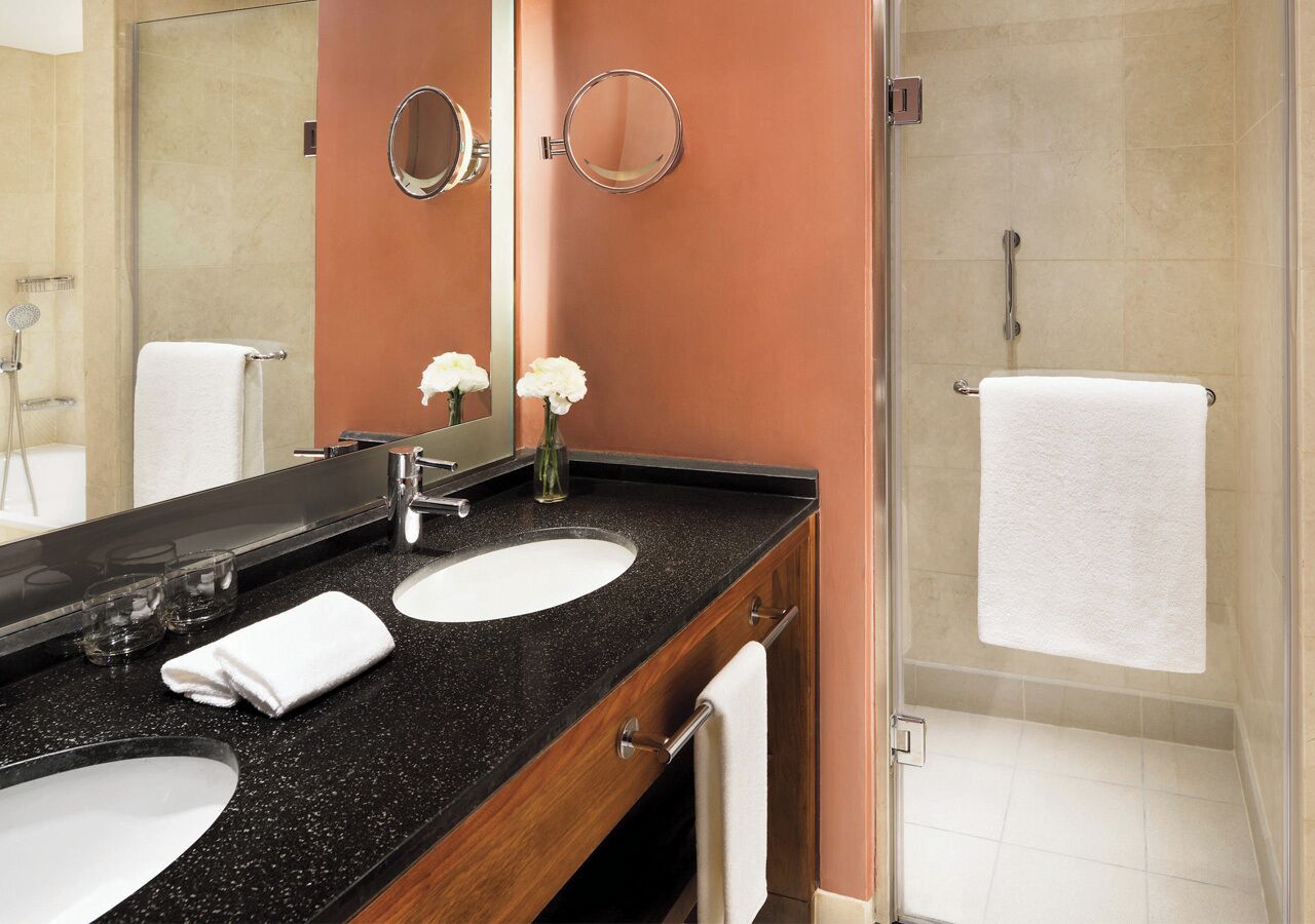 A bathroom with two sinks, a mirror, and a shower.