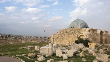 An ancient stone structure with a dome, surrounded by ruins and a cityscape in the background.