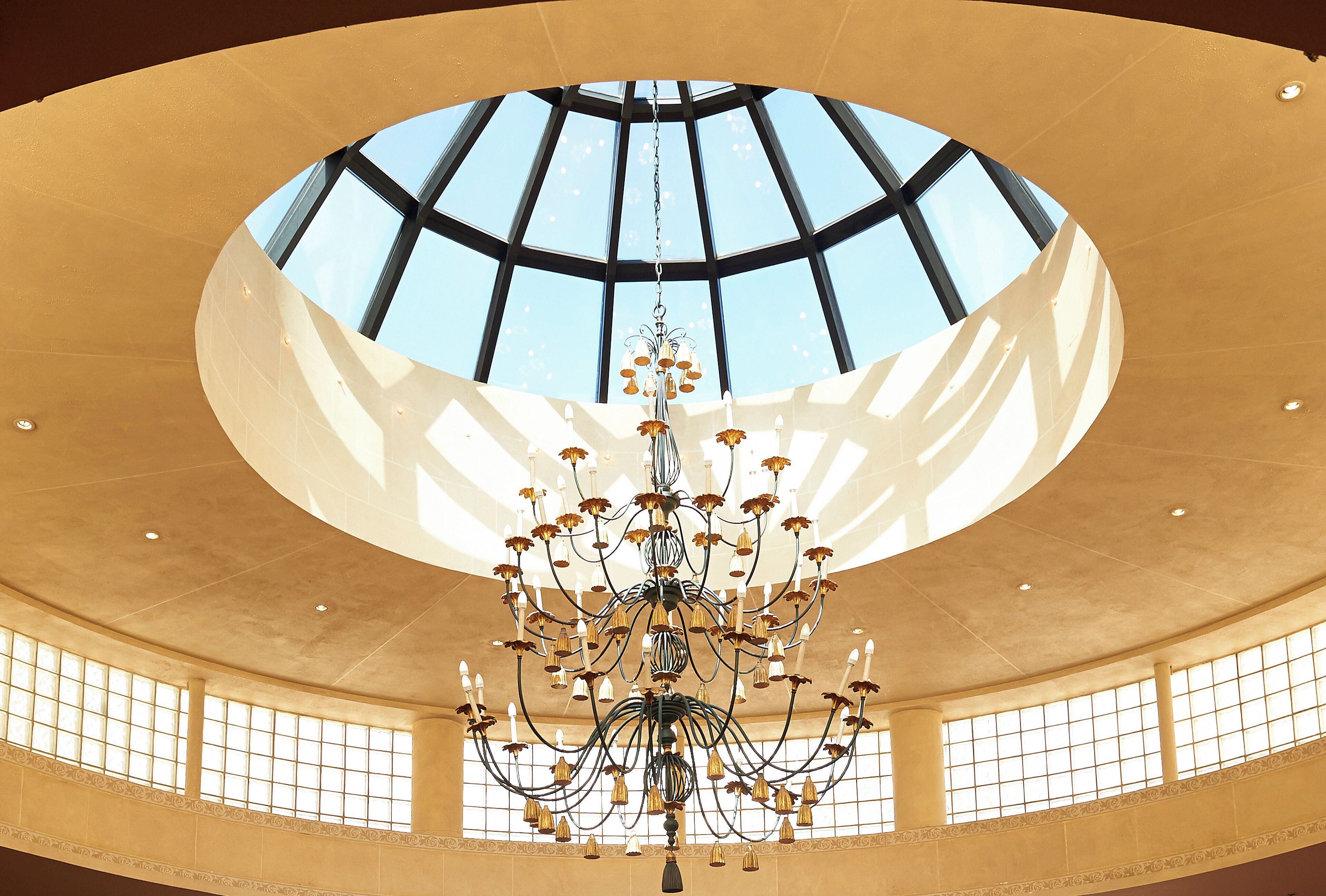 A grand interior with a large, circular skylight and a chandelier with multiple light fixtures.