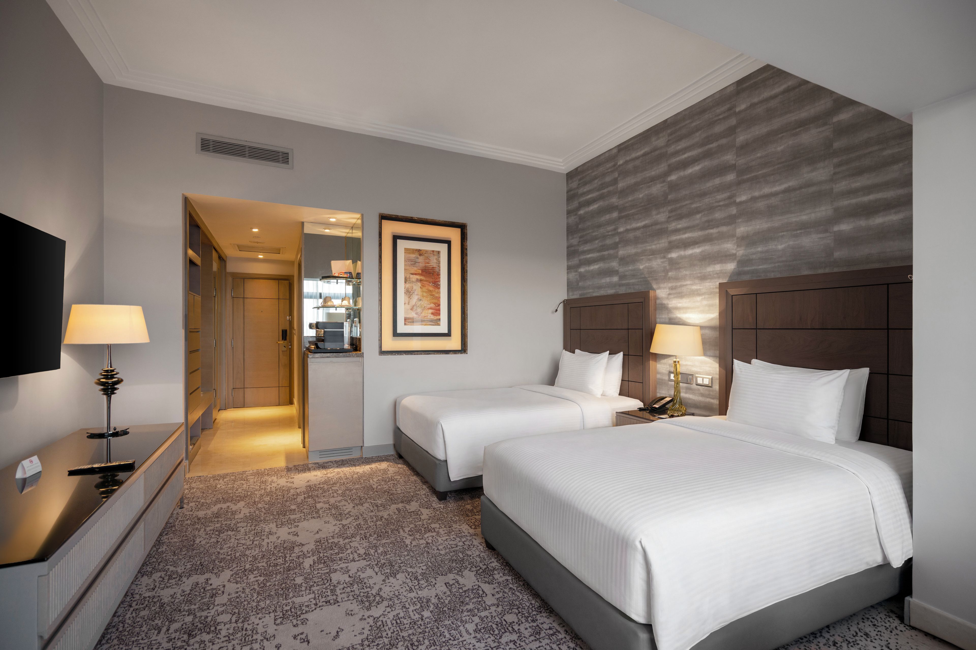 A hotel room with two beds, a flat-screen TV, a desk with a lamp, and a framed picture on the wall.