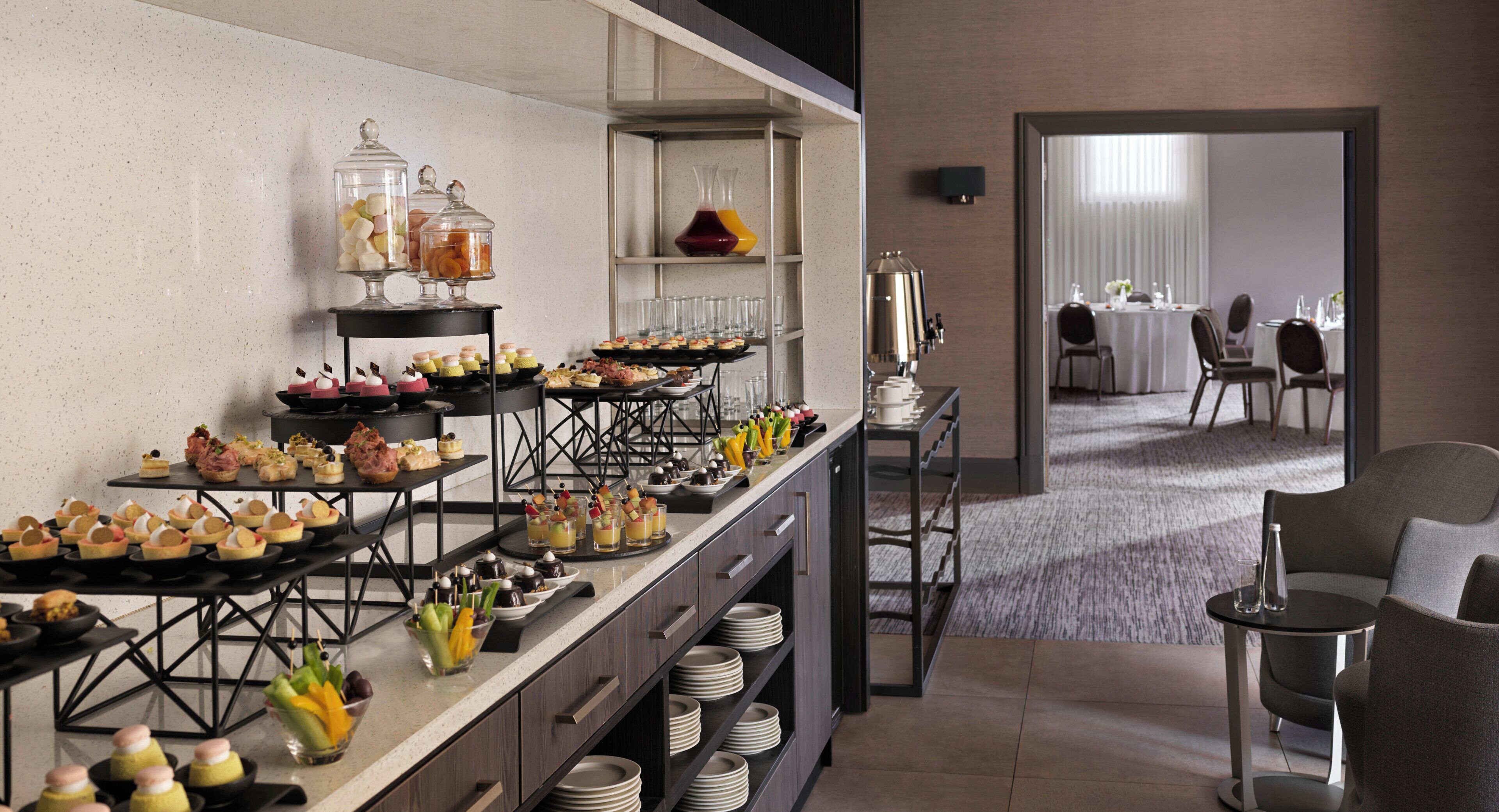 A buffet setup with various food items and drinks, a coffee station, and a seating area with tables and chairs.