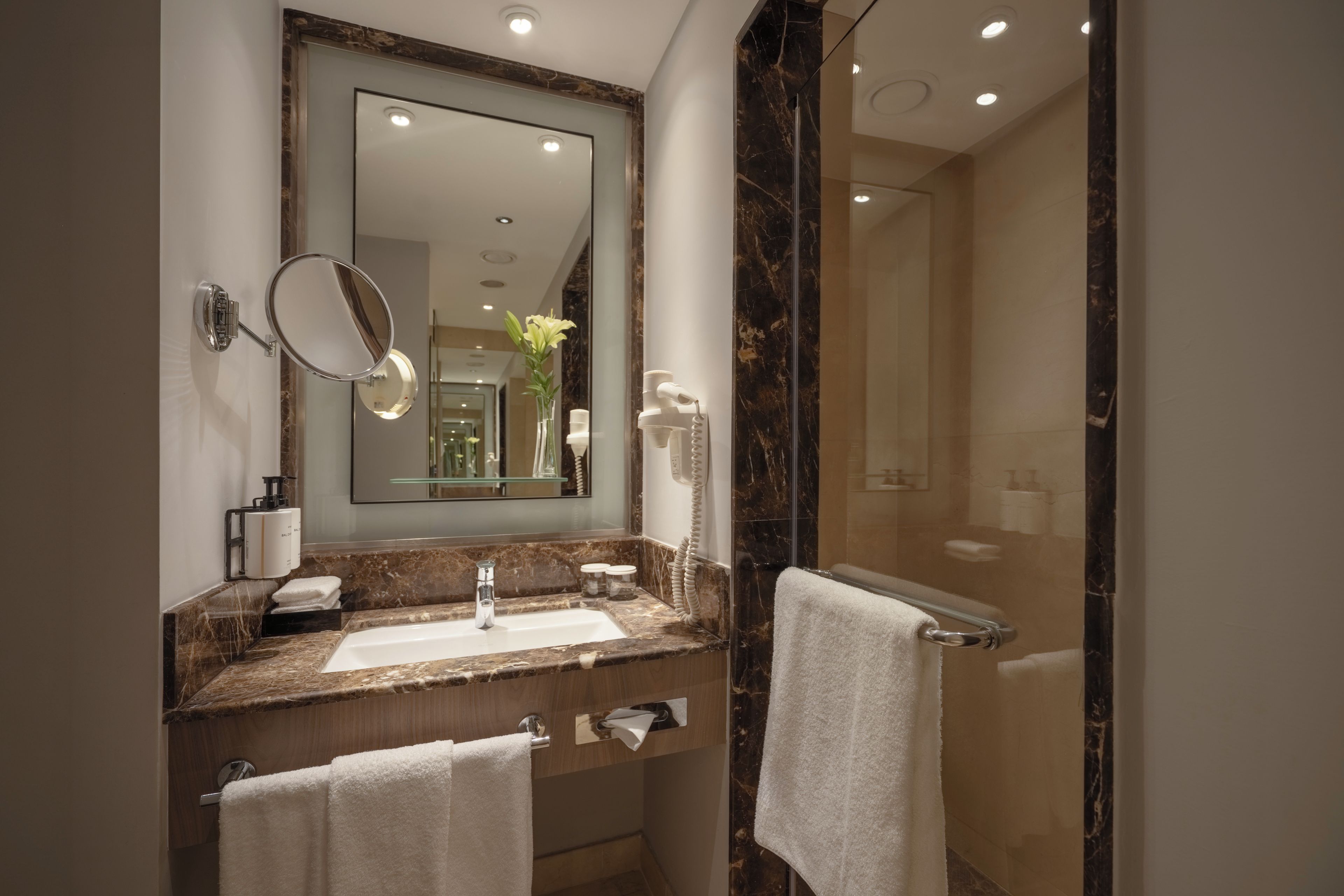 A bathroom with a large mirror, a sink, a towel rack, and a shower area.
