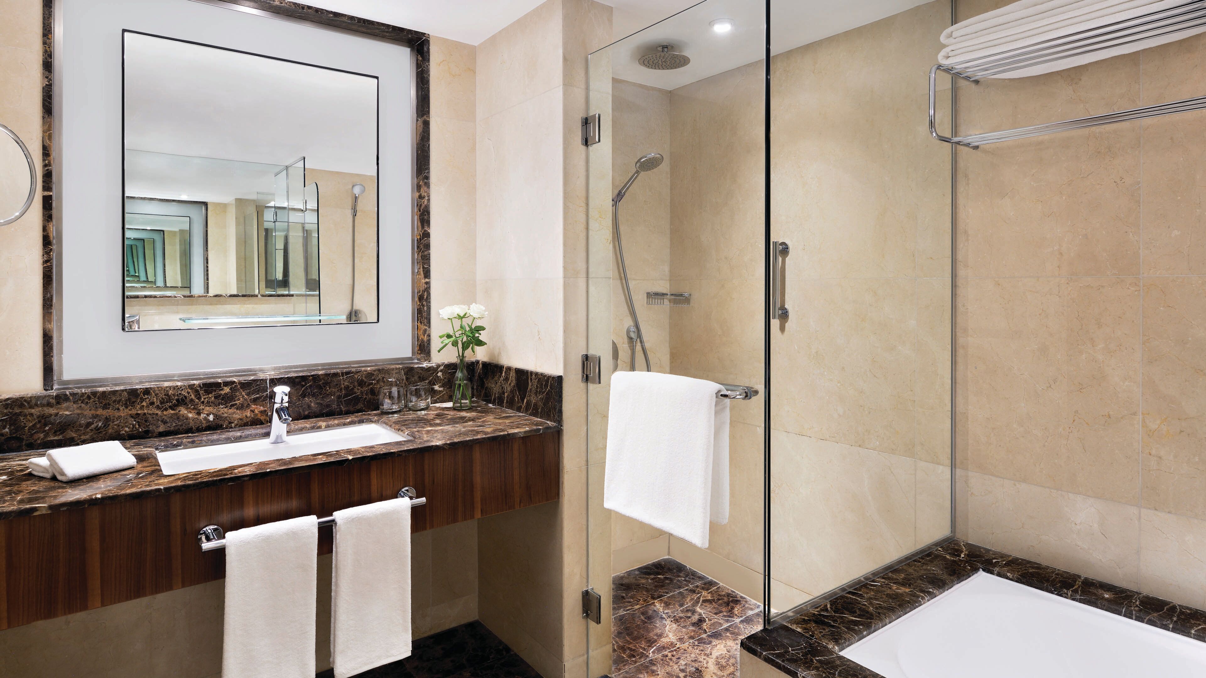A modern bathroom with a marble countertop, a glass-enclosed shower, and a large mirror.