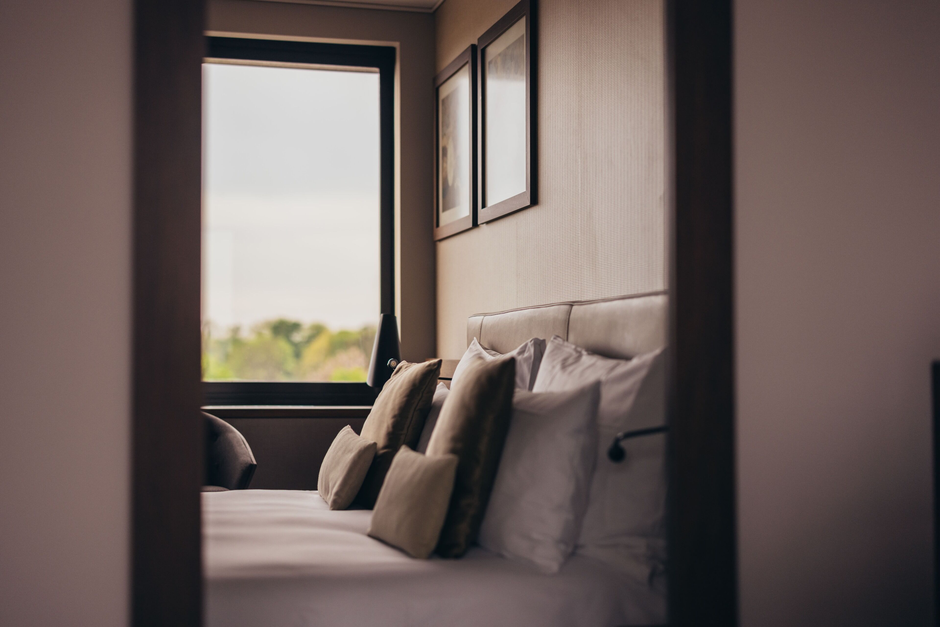 Une chambre à coucher avec un lit, des oreillers, une fenêtre et des tableaux encadrés accrochés au mur.