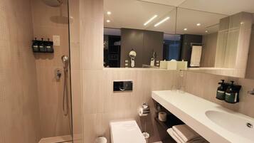 Un baño moderno con ducha de vidrio, inodoro, lavamanos y un espejo grande.