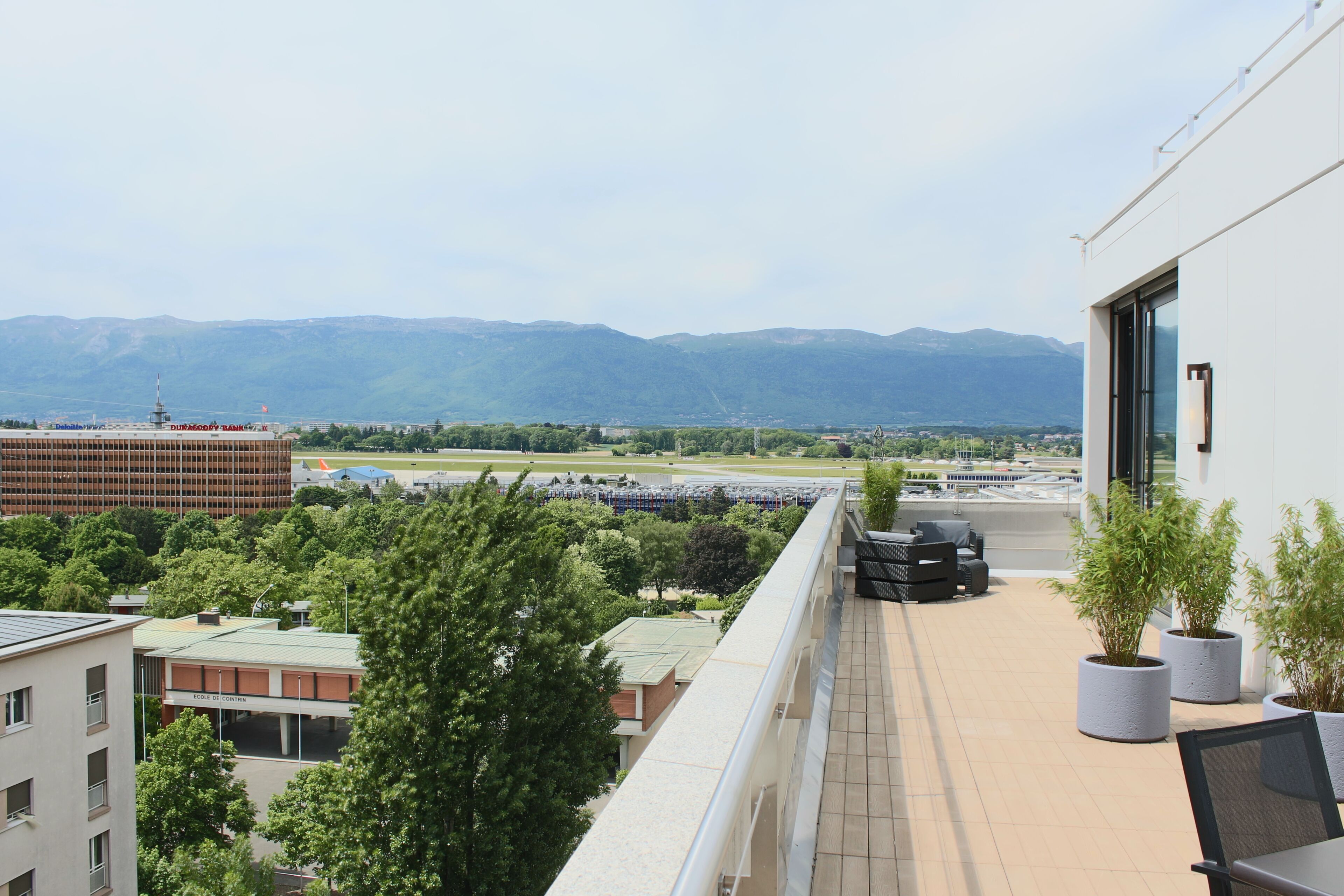 A balcony with a view of mountains, a parking lot, and a building with a sign.