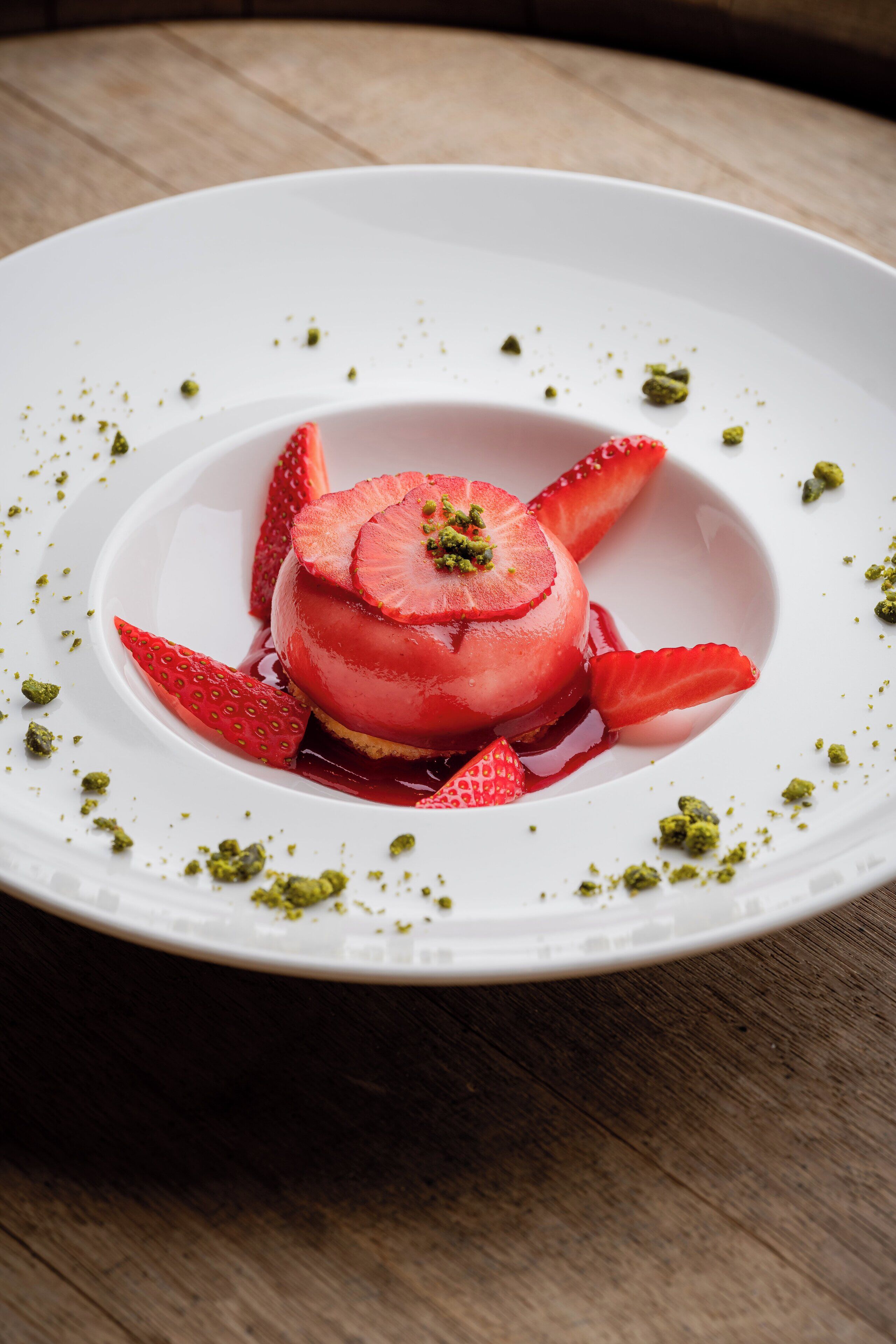 A dessert on a white plate with strawberries and pistachio garnish.