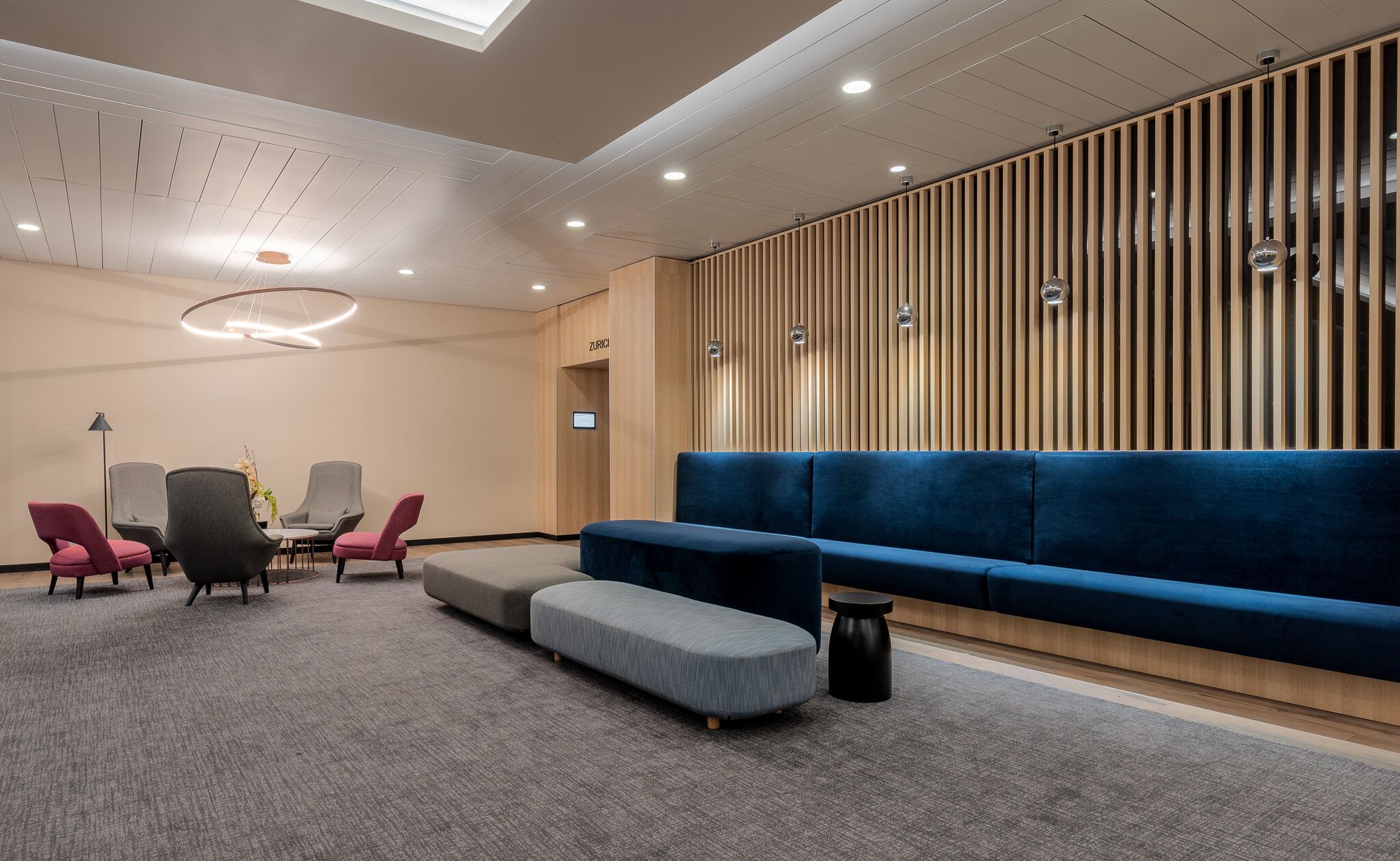 A modern waiting area with a blue sofa, grey chairs, and a small table.