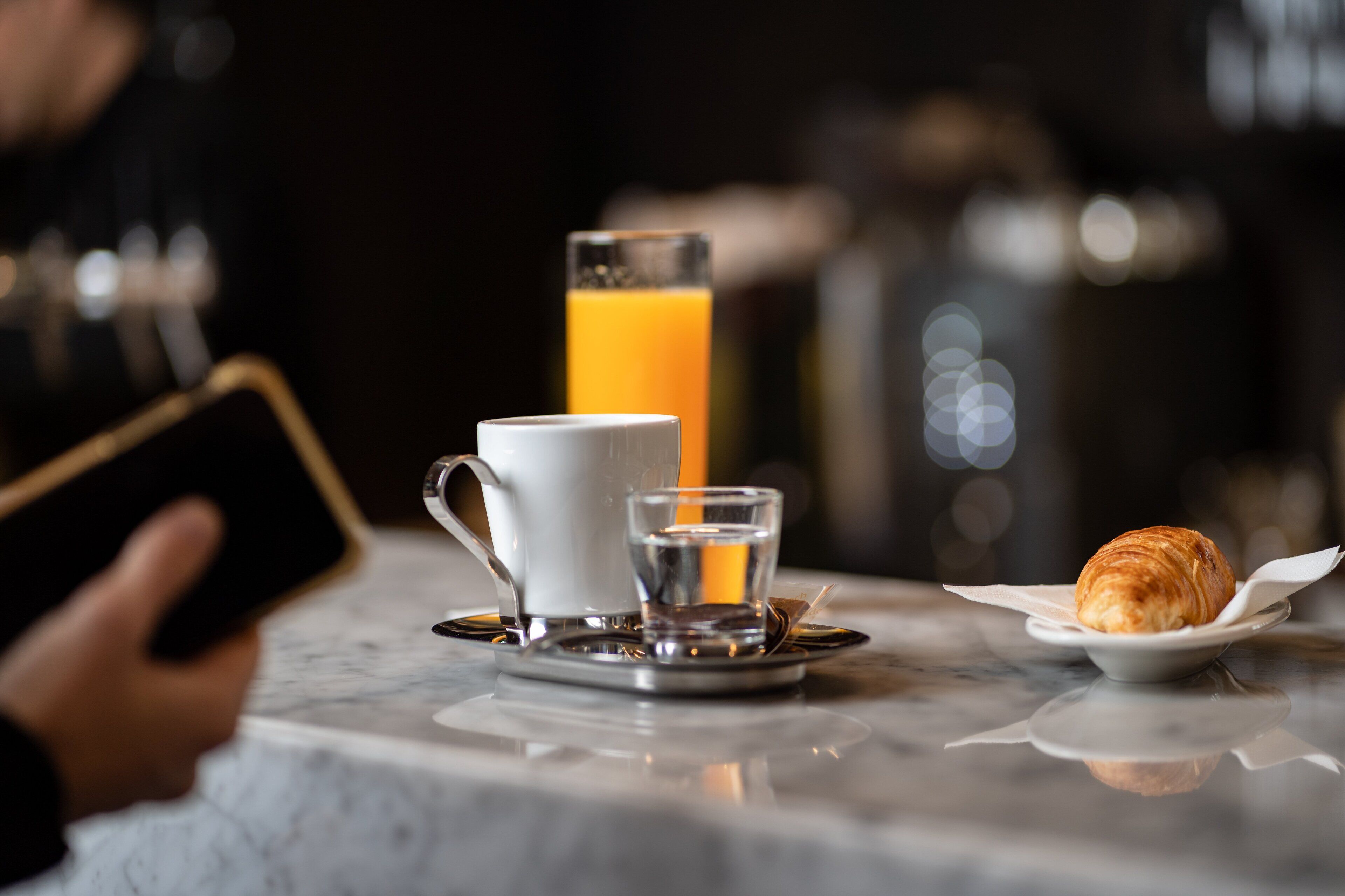 A breakfast setting with a cup, a glass of orange juice, a small glass of water, and a croissant on a plate.