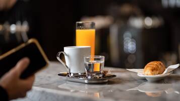 A breakfast setting with a cup, a glass of orange juice, a small glass of water, and a croissant on a plate.