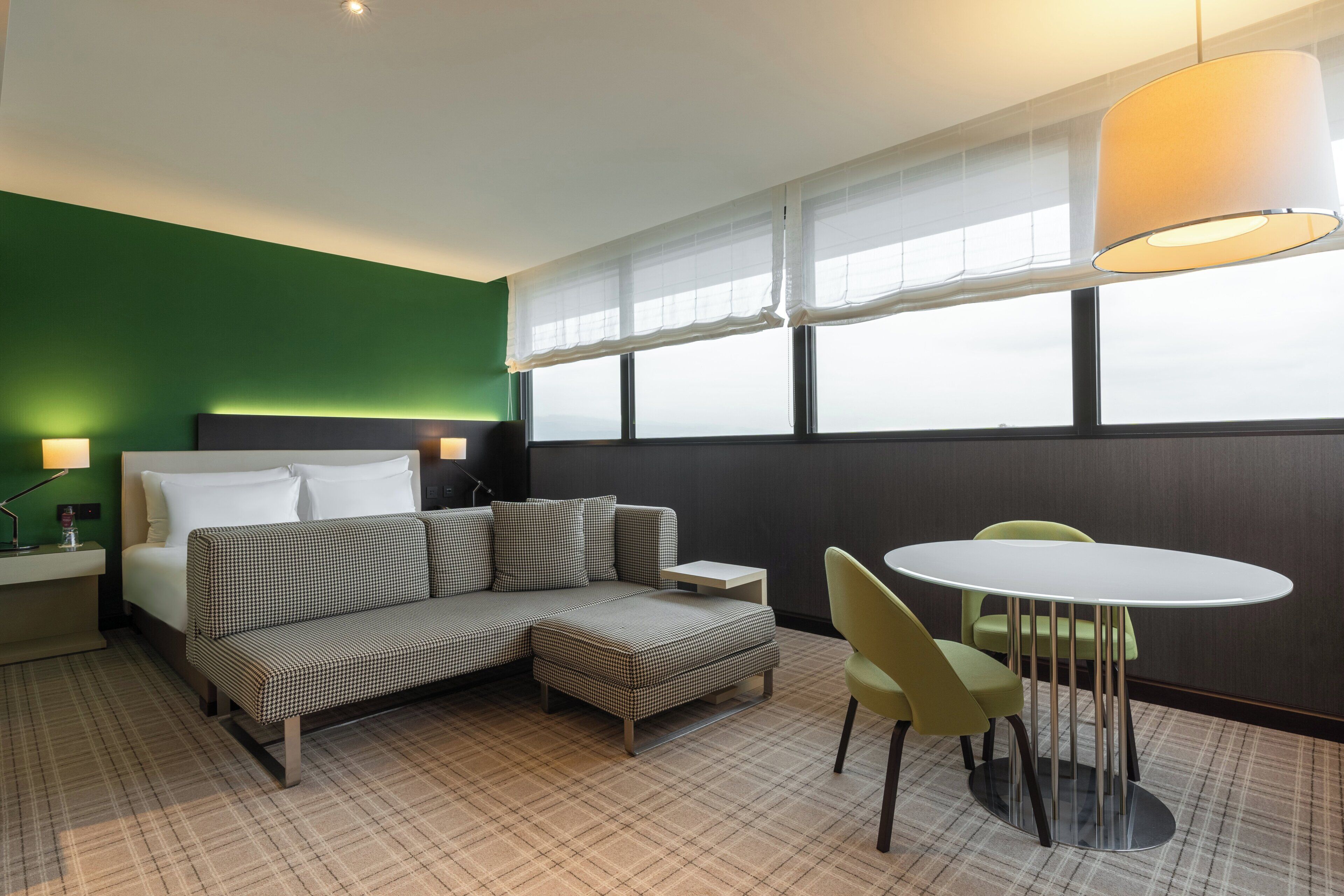 A hotel room with a bed, a sofa, an ottoman, a table, and chairs.
