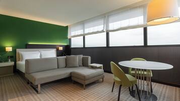 Una habitación de hotel con una cama, un sofá, un reposapiés, una mesa y sillas.