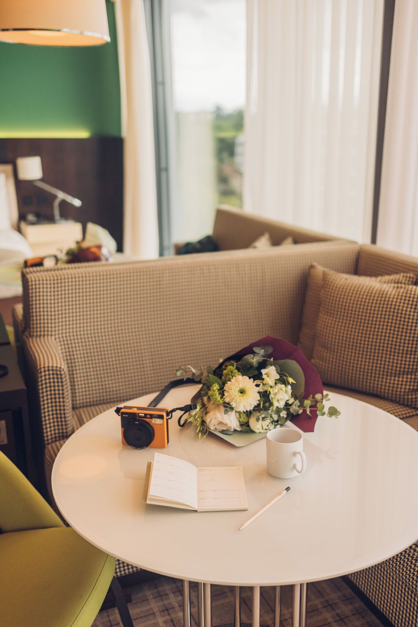 A round white table with a camera, a notebook, a pen, and a bouquet of flowers.
