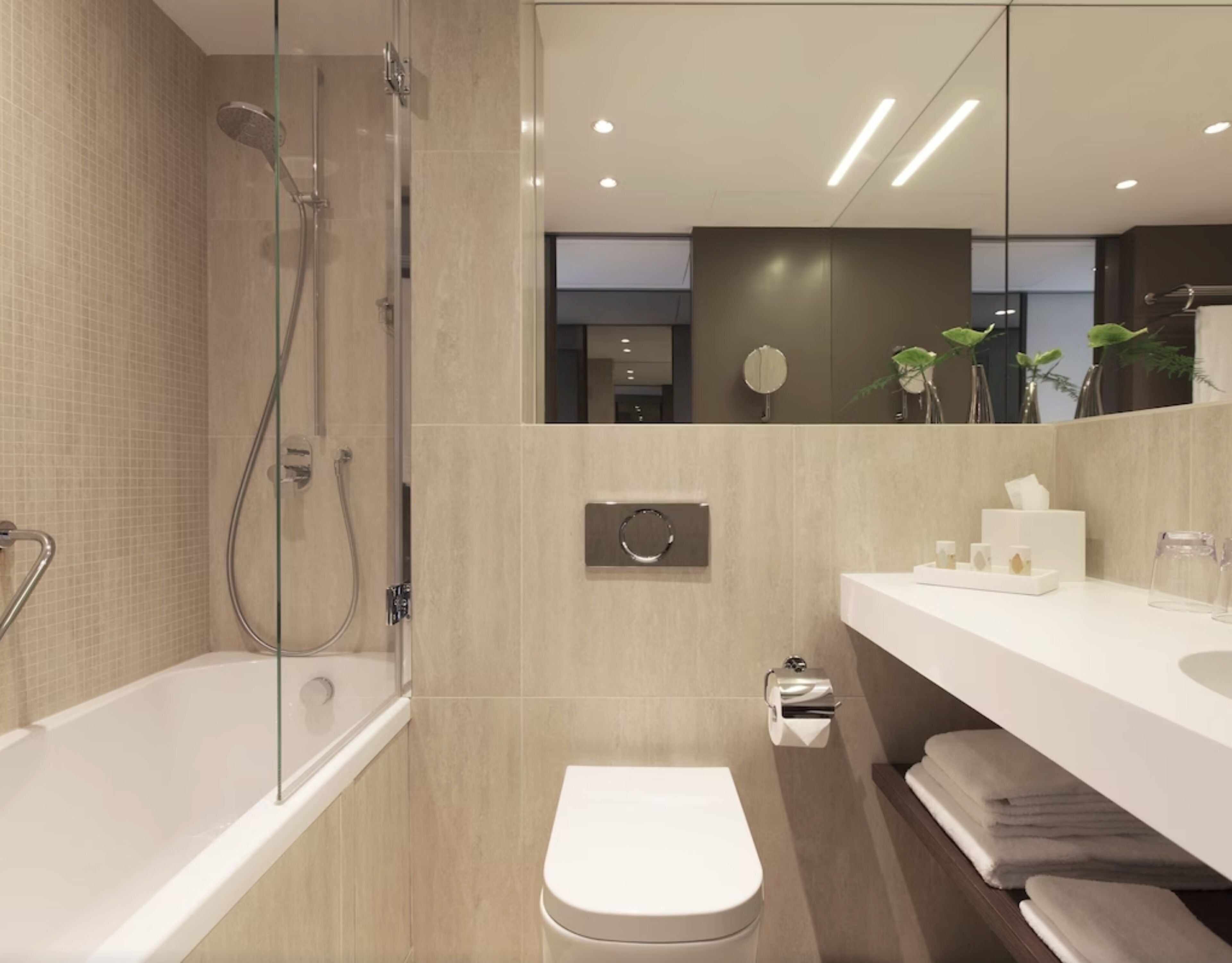 A modern bathroom with a glass-enclosed shower, a white toilet, and a vanity with a mirror and toiletries.